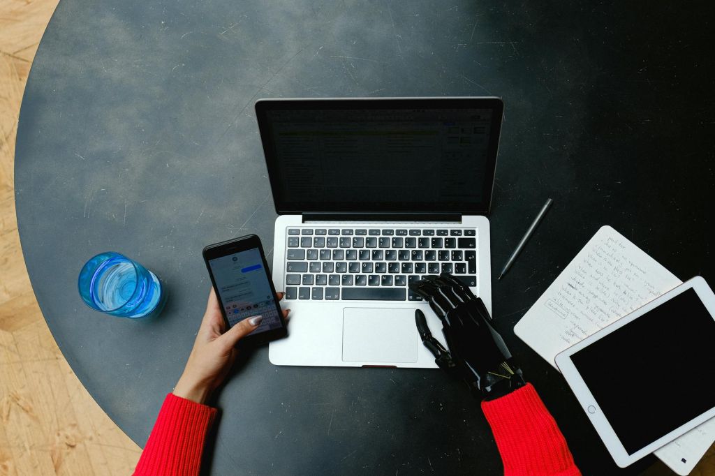 woman with prostethic hand using laptop and smartphone