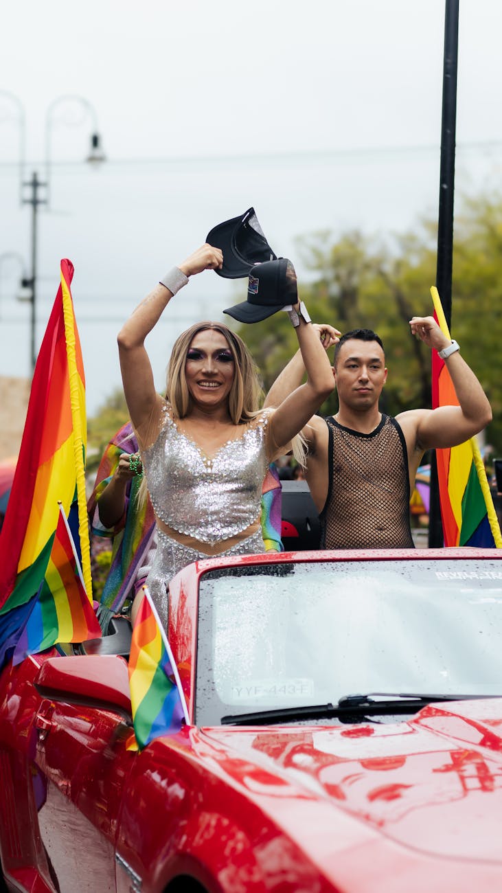 people riding in a convertible draped in lgbt flags at a pride parade