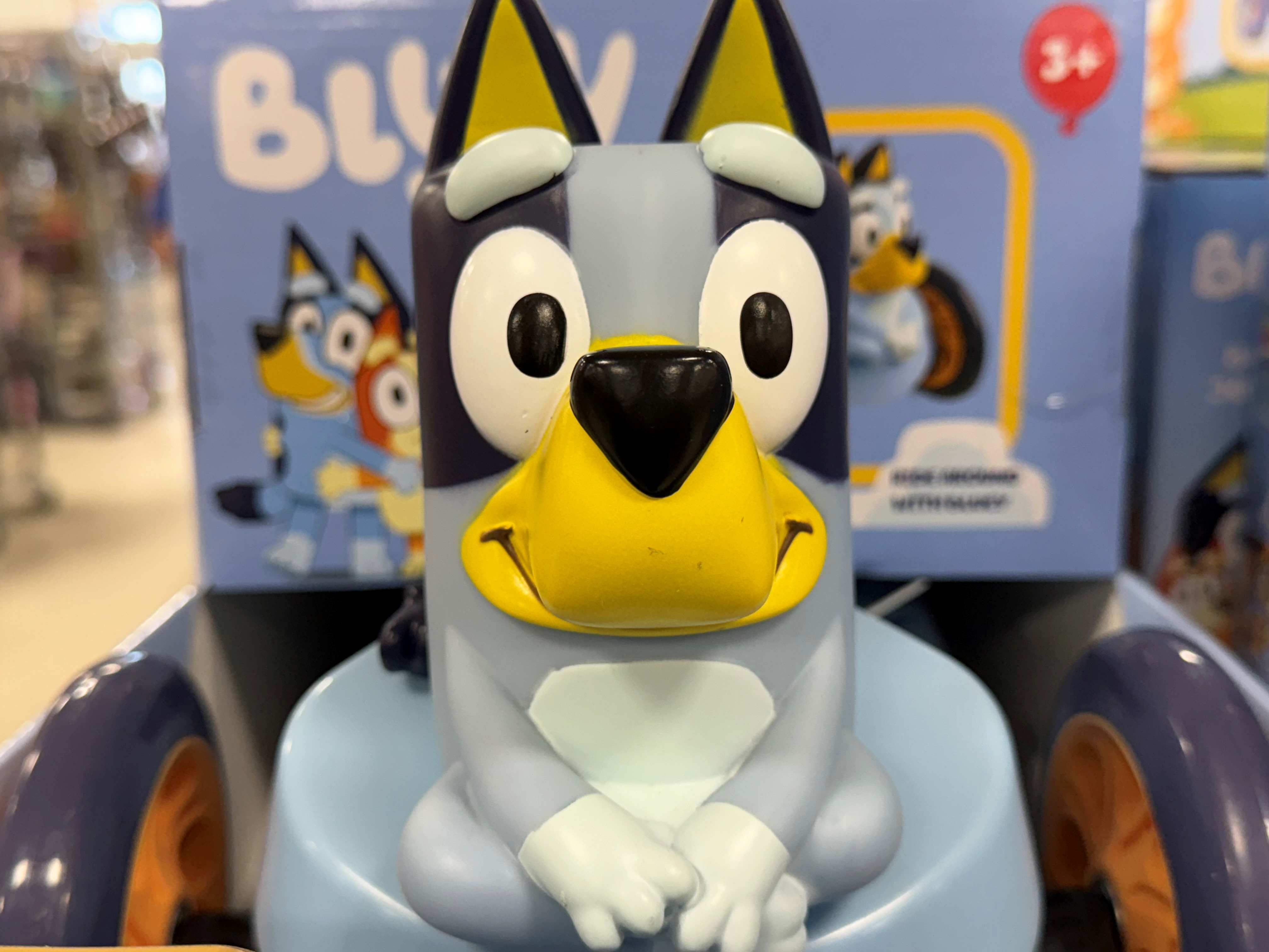 A plush toy of a black and white dog-like character with a yellow beak and large eyes, sitting on a blue background with other similar characters.