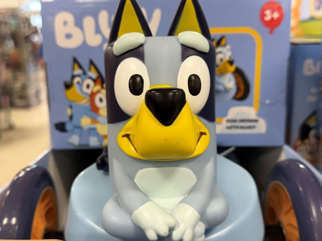 A plush toy of a black and white dog-like character with a yellow beak and large eyes, sitting on a blue background with other similar characters.