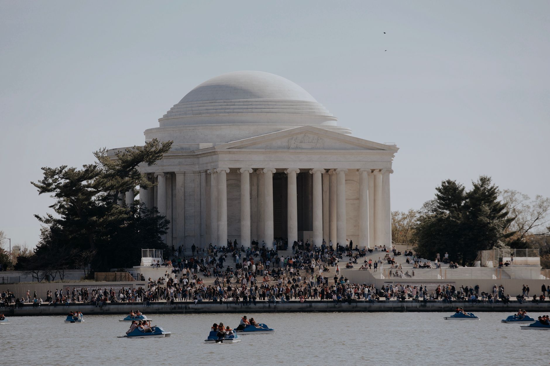 people boating on river and crowd standing near thomas jefferson memorial