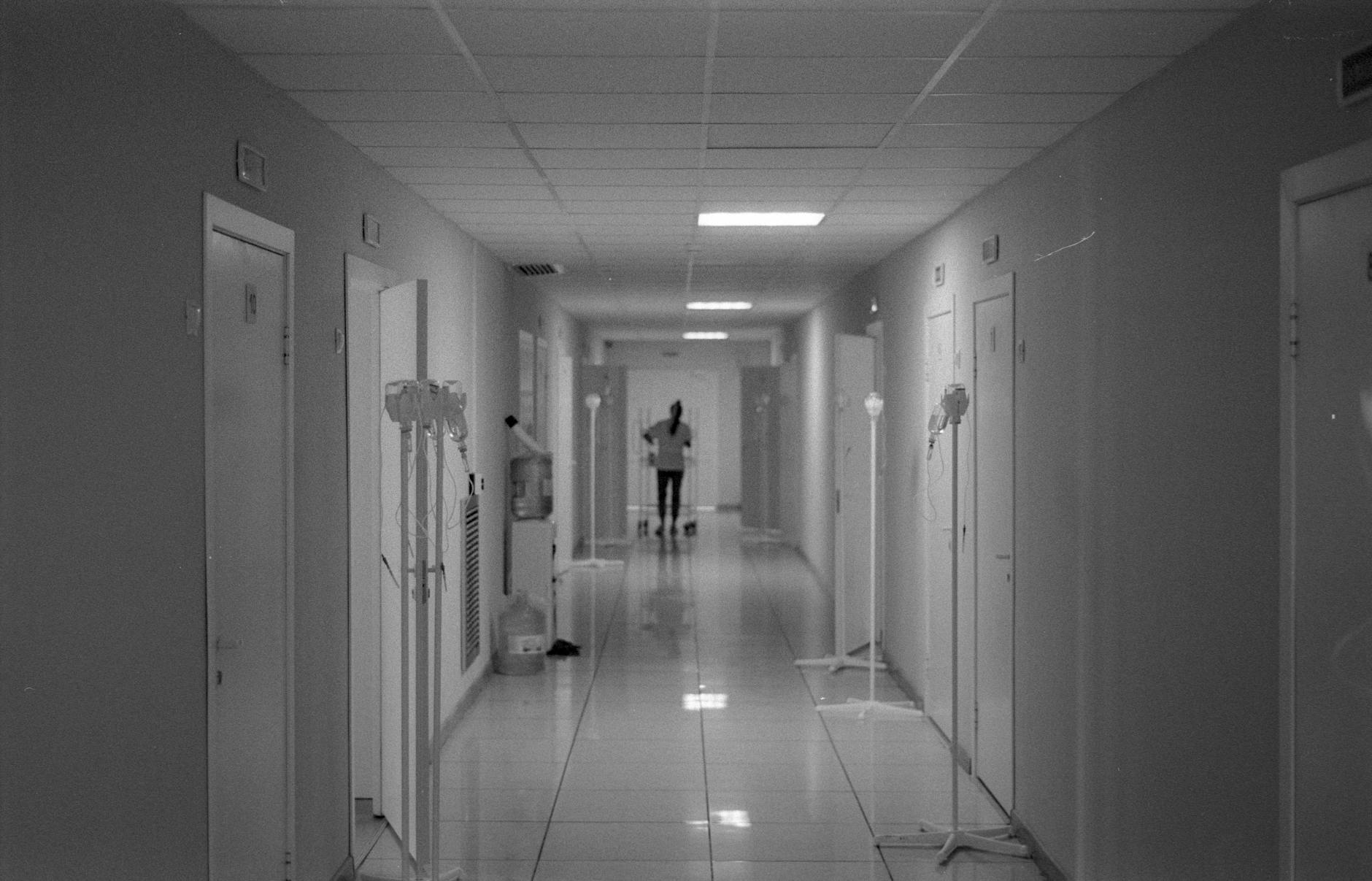 black and white photo of nurse standing at end of hospital hallway