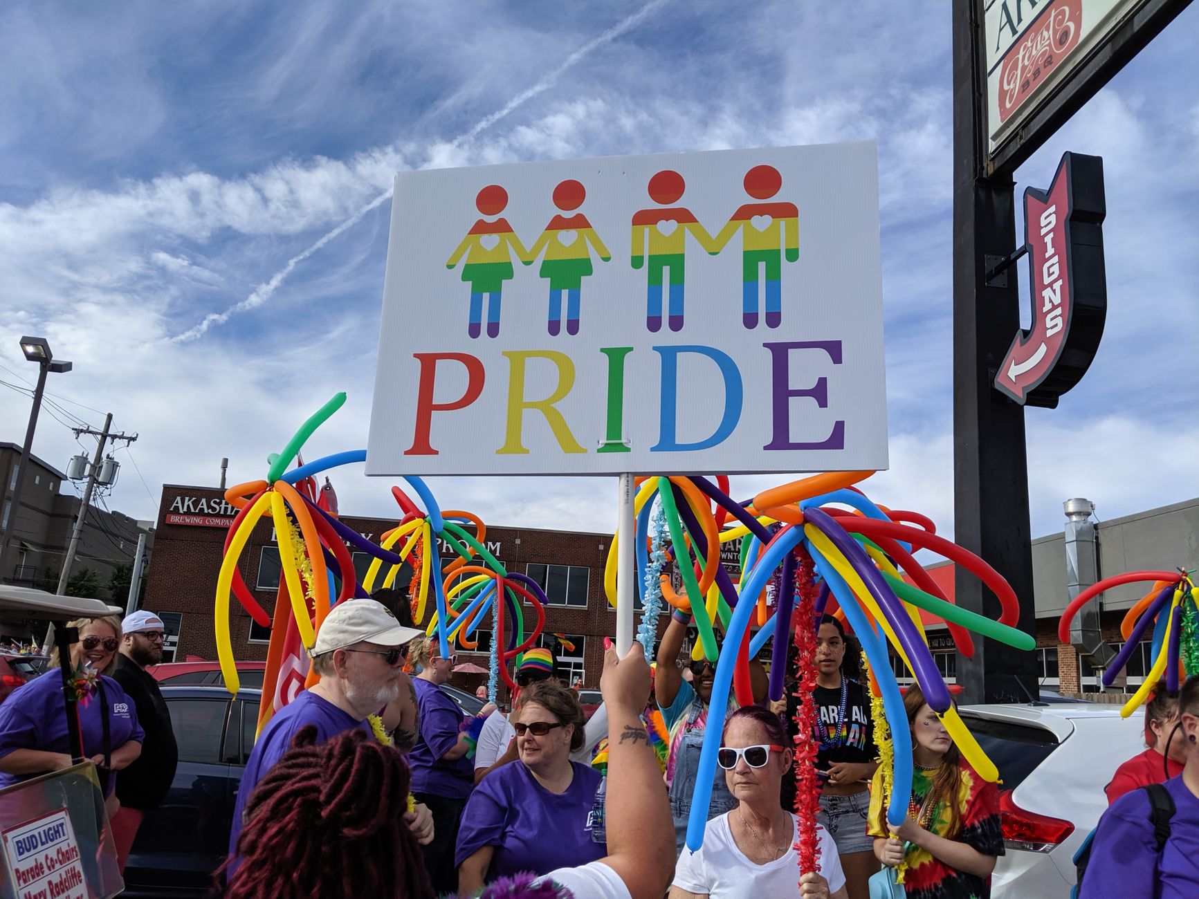 people carrying rainbow balloons and pride board signs