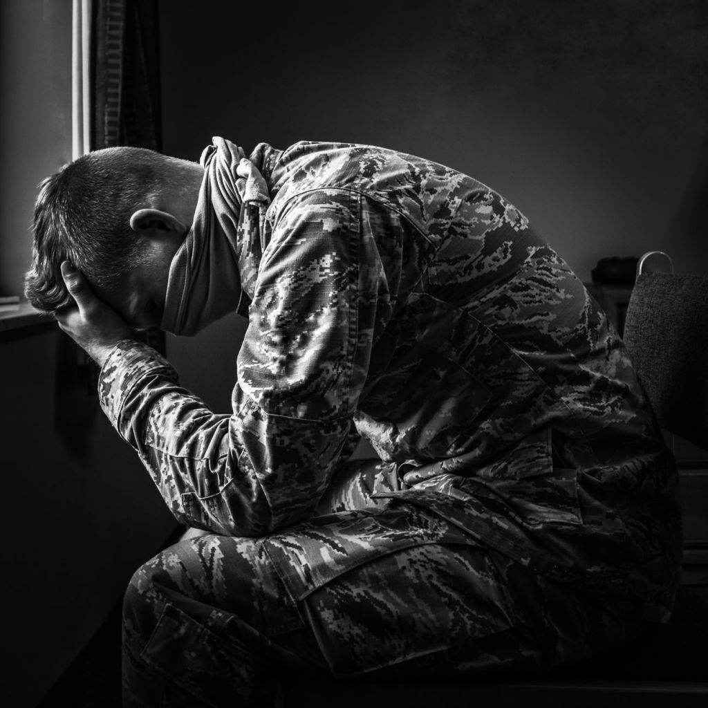 young soldier in uniform sitting and covering face with hand