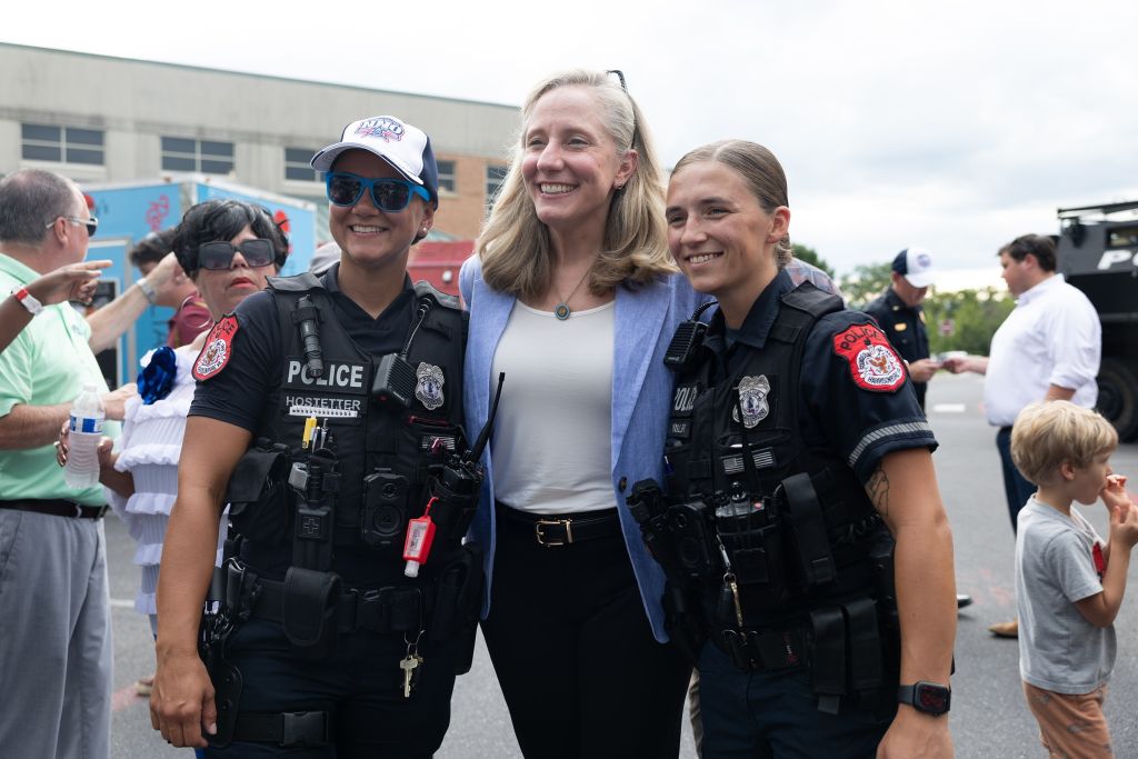 Two female police officers in uniform standing with a woman in a light-colored jacket, smiling and posing for a photo.